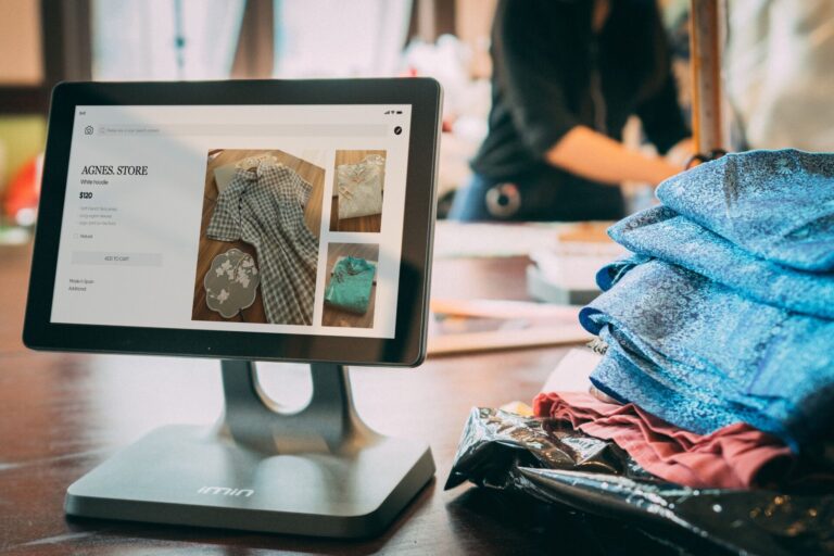Modern digital point of sale terminal in a boutique retail store displaying e-commerce product catalog next to folded apparel
